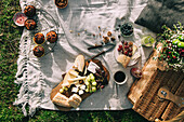 Flatlay picnic scene with a basket and flowers, juice, grapes, cheese and baguette