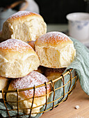 Homemade milk and cream cheese buns in a basket with a cloth next to a window