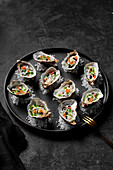 Freshly shucked oysters with buttermilk dressing, salmon roe, balsamic pearls and herb oil sitting on rock salt on a black plate