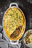 Shepherds Pie topped with mashed potatoes in white dutch oven with serving on plate, close shot