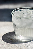 Glass of pure water with ice cubes in hot summer day on concrete table background