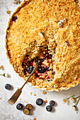 A bowl of apple and blueberry crumble that has had a portion taken out and the serving spoon left in the bowl.