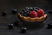 Pastry basket with blueberries and raspberries. Cake on a dark background