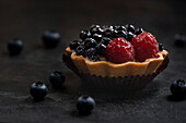 Gebäckkorb mit Heidelbeeren und Himbeeren. Torte auf dunklem Hintergrund