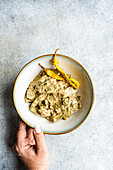 Top view of cropped hand holding a plate of Georgian green beans with walnut sauce against light background