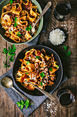 Medium shot of two bowls (black and green) of fresh pasta noodles with meat and tomato ragu with forks, parsley, red wine and grated cheese