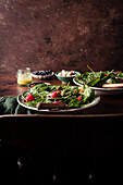 A healthy green salad with spinach and apple and raspberries in two bowls on a wooden table