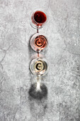 Flat-lay of red, rose and white wine in glasses on grey stone background. Wine bar, winery, wine degustation concept. Minimalistic trendy photography.