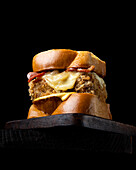 From below appetizing burger with fresh bread cheese and bacon served on a wooden board on a black background