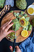 A woman's hand cuts off the pointed tips of the lower leaves of an artichoke