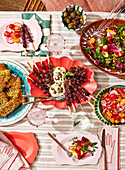 Ein Picknick mit Salat an einem Tisch im Freien, mit frischem Obst und Gebratenem, auf einem gestreiften Tischtuch