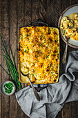 Cauliflower cheese in a baking dish on wood table with chives and serving on plate