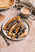Crêpes drizzled with melted dark chocolate on a ceramic plate