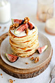 Pancake stack decorated with cream, figs, walnuts and honey on a rustic base