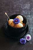 Vanilla ice cream scoops with edible flowers in a black bowl on a dark background