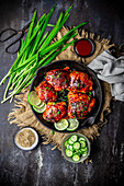 Old cast-iron pan with savoury glazed chicken thighs with sauce, cucumber slices and chives on top