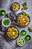 Arrangement of dark bowls with Japanese chicken, egg and rice, with green sake cups and bowl with cucumber slices