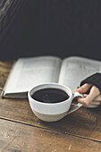 A woman's hand holds a black coffee with a book in it