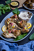Fried artichokes served on an oval plate with a bowl of dipping sauce on the side, photographed from the front