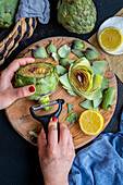 Women's hands peel the stem of an artichoke with a peeler