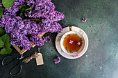 Tasty black tea in vintage white cup on mint green concrete table with aromatic lilac flowers