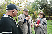 Calm mature men and women in traditional dress chatting and drinking mate while spending time together in a meadow in the park