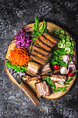 Sliced crispy pork belly on a wooden plate with a knife and colourful vegetable garnishes