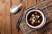 Miso soup with tofu, seaweed and sesame seeds in a bowl on a wooden base