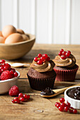 Schokoladen-Cupcakes mit roten Früchten auf Holztisch