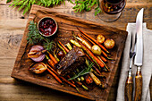 Grilled venison steak with baked vegetables and berry sauce and red wine on wooden background