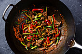 Stir-fry beef meat with vegetables in wok pan on dark background close up