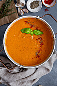 Roasted tomato soup garnished with spices and fresh basil leaves in a pot, black pepper, paprika, garlic and thyme on the side.