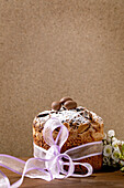 Hausgemachter italienischer traditioneller Oster-Panettone-Kuchen, verziert mit Schokoladeneiern, rosa Schleife und blühenden Kirschbaumblüten auf Holztisch stehend. Traditionelles europäisches Ostergebäck. Platz zum Kopieren