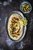Hummus swirled on oval metal plate with charred scallions, lemon slices and olive oil
