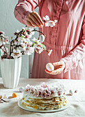 crepe cake or blini cake for Easter party, rose pink background, almond flowers, rose pink background, woman hands