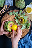 Women's hands rubbing the cut surface of an artichoke with lemon