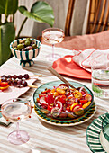 Ein Picknick mit Salat an einem Tisch im Freien, mit frischem Obst und Gebratenem, auf einem gestreiften Tischtuch