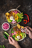 Chili con carne in two bowls with garnishes, pickled red onions, male hands with spoon on dark background