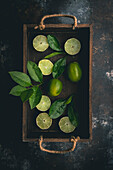 Limes, cut and whole, and Lime Leaves in wood box on dark background