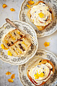 Three lemon rolls on plates, one of which is cut in half to reveal the lemon curd and dried fruit filling