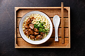Langsam gekochtes Rinderfleisch mit asiatischen Nudeln in Brühe in Holztablett auf dunklem Hintergrund