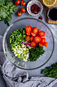 Chopped onions, green onions, parsley, dill and halved cherry tomatoes in a glass bowl.