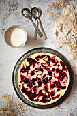 A whole baked cheesecake with blackcurrant compote ripple through it with a jug of pouring cream at the side.
