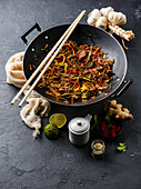 Asian fast food Stir fry noodles soba with beef and vegetables in a wok pan on a dark stone background