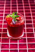 Strawberry and hibiscus mind basil spritz tea on a red tiled background with garnish