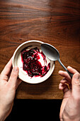 Bowl of yoghurt and blackberry compote on antique wooden table with silver spoon