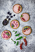 Arrangement aus vier kleinen Törtchen, gefüllt mit Beerencreme, dekoriert mit frischem Obst und Minze