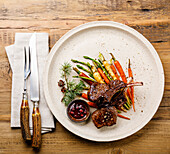 Grilled Venison Ribs with baked vegetables and berry sauce on wooden background