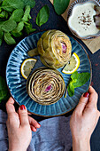 Woman serving steamed artichokes with her hands on a dark blue plate