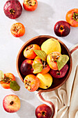 Pomegranates, persimmons, pears and apples in a bowl on a neutral background